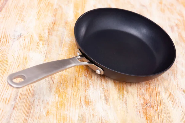New non-stick frying pan on a wooden table. Kitchen utensils