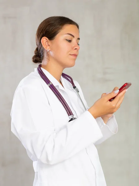 Sorrindo Médico Feminino Olhando Para Cima Algo Seu Telefone — Fotografia de Stock