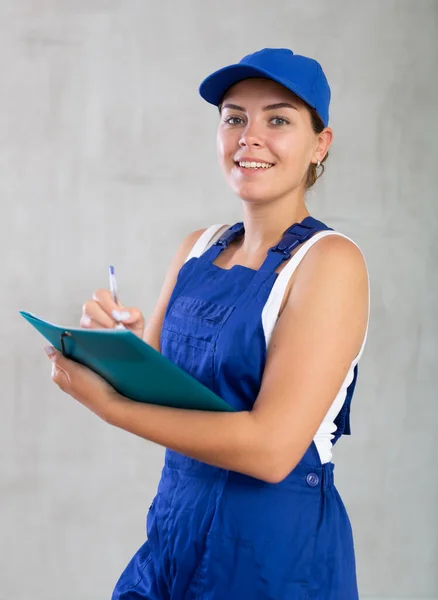 有兴趣的女机修工穿着蓝色工作服写下订单 — 图库照片