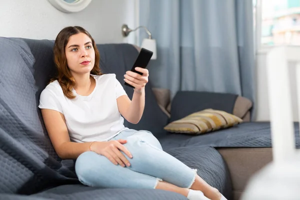 Νεαρή Γυναίκα Κάθεται Έναν Καναπέ Ένα Διαμέρισμα Βλέποντας Τηλεόραση Κρατώντας — Φωτογραφία Αρχείου