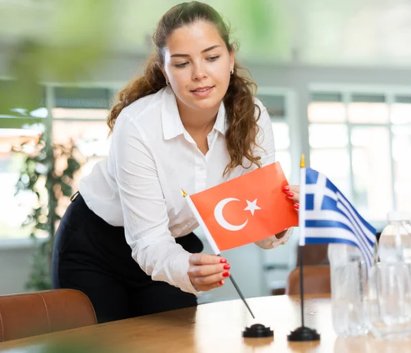 助理女孩为国际谈判和领导人会议准备办公室 女士把希腊和土耳其的小型国旗摆上桌 后续行动 — 图库照片