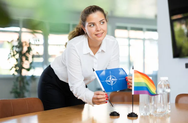 Młoda Kobieta Ubraniu Biznesowym Stawia Flagi Nato Lgbt Stole Negocjacyjnym — Zdjęcie stockowe