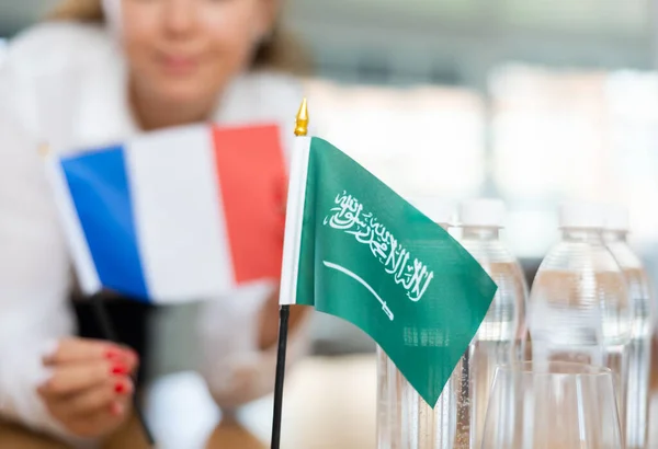 沙乌地阿拉伯的小国旗放在桌子上 旁边放着一瓶水和法国国旗 旁边坐着一位积极的年轻女子 — 图库照片