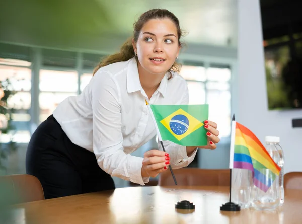 アシスタント ガールは 国際交渉や指導者会議の事務局を準備する 女性はテーブルの上にLgbtとブラジルのミニチュアフラグを設定します — ストック写真