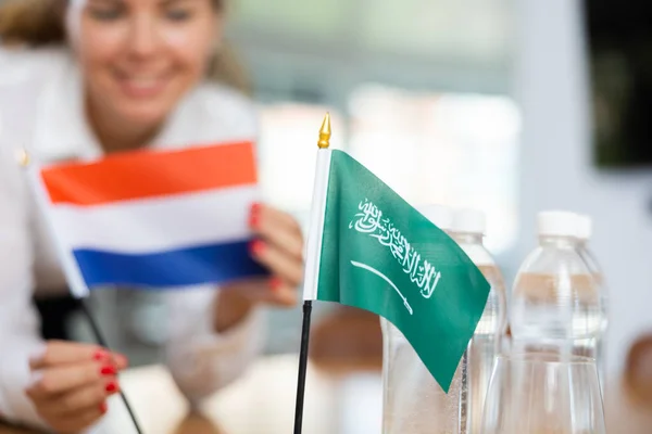 正の若い女性によってそれの隣に置かれたオランダの水とフラグのボトルとテーブルの上にサウジアラビアの小さなフラグ — ストック写真