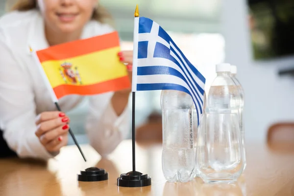 难以辨认的妇女为国际谈判和领导人之间的沟通讨论准备了空间 女士将希腊和西班牙国旗的缩影摆上桌 — 图库照片