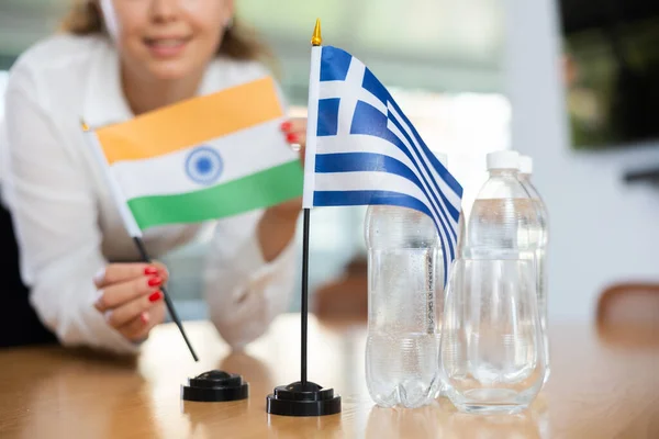 难以辨认的妇女为国际谈判和领导人之间的沟通讨论准备了空间 女士将希腊和印度国旗的缩影摆上桌 — 图库照片