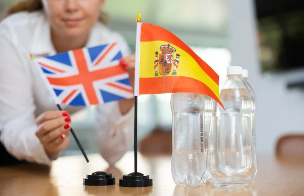 ビジネス服の若い女性はオフィスで交渉テーブルの上に英国とスペインのフラグを置きます — ストック写真