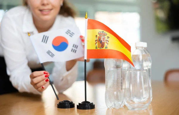 正の若い女性によってそれの隣に置かれた韓国の水とフラグのボトルとテーブルの上にスペインの小さな旗 — ストック写真