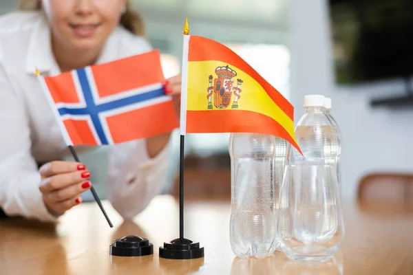 正の若い女性によってそれの横に置くノルウェーの水とフラグのボトルとテーブルの上にスペインの小さな旗 — ストック写真