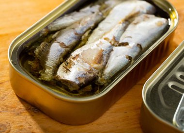 Open can of sardines preserves in oil on wooden table clipart