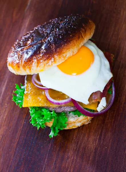 Pyszny Burger Jajkiem Smażonym Bekonem Serem Cebulą Sałatą Drewnianym Tle — Zdjęcie stockowe