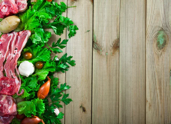 Raw mutton meat, fresh vegetables and greens on wooden background, with copyspace