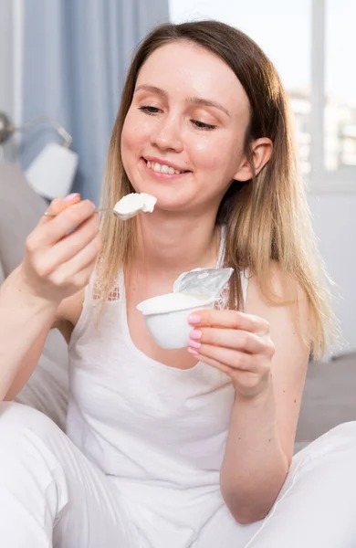 在家里沙发上摆弄酸奶的快乐女性的画像 — 图库照片
