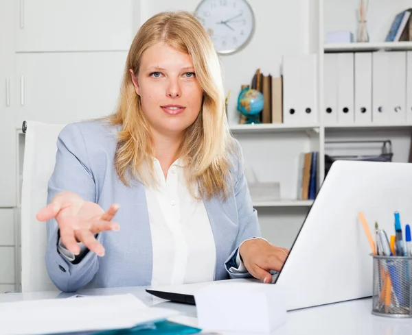 自信的女商业顾问双手叉腰坐在办公室桌旁做手势 — 图库照片
