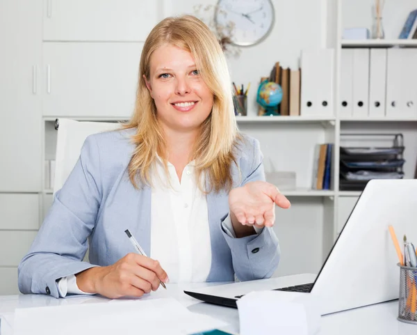 自信的女商业顾问双手叉腰坐在办公室桌旁做手势 — 图库照片