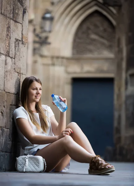 Leende Ung Kvinna Sitter Nära Gamla Stenvägg Dricksvatten Från Flaska — Stockfoto