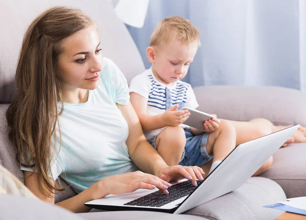 Mulher Satisfeita Está Trabalhando Produtivamente Atrás Laptop Enquanto Criança Brincando — Fotografia de Stock