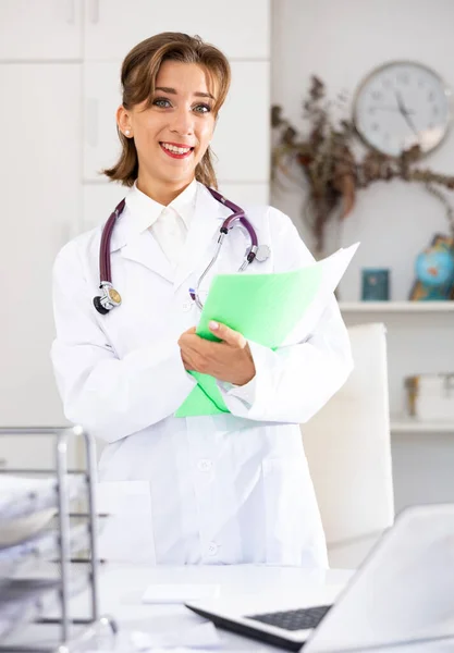 Pozytywna Kobieta Lekarz Stojący Jej Biurze Trzymając Teczkę Papieru Patrząc — Zdjęcie stockowe