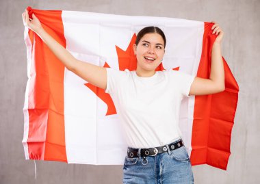 Young positive woman holding national flag of Canada in her hands clipart