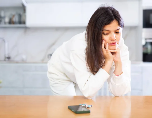 Üzgün Genç Siyah Saçlı Bir Kadın Telefon Bekliyor Mutfaktaki Masaya — Stok fotoğraf