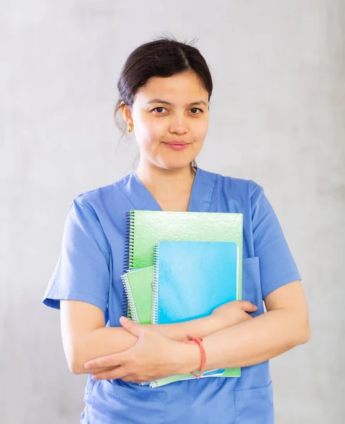 穿着蓝色制服站在室内灰色背景笔记本的年轻女医生的画像 — 图库照片