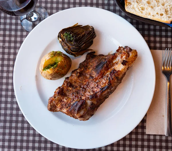 美味的烤牛肉排骨与煮土豆和烤洋蓟一起放在盘子里 受欢迎的西班牙配餐 — 图库照片