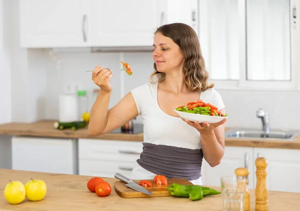 家庭で台所でサラダを食べる正の白人女性の肖像画 女性は新鮮な野菜サラダを調理しています — ストック写真
