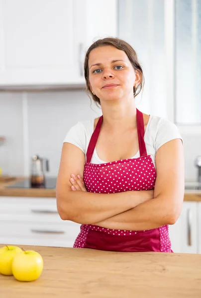 台所に立っているエプロンを身に着けている若い主婦を笑顔 カメラにポーズ — ストック写真