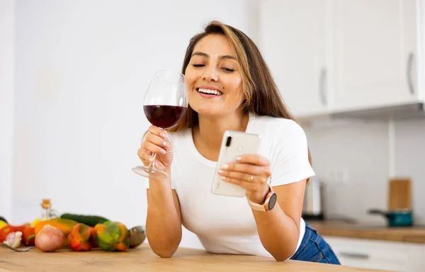 Szczęśliwa Gospodyni Domowa Szklanką Czerwonego Wina Kuchni Czytanie Wiadomości Ekranie — Zdjęcie stockowe