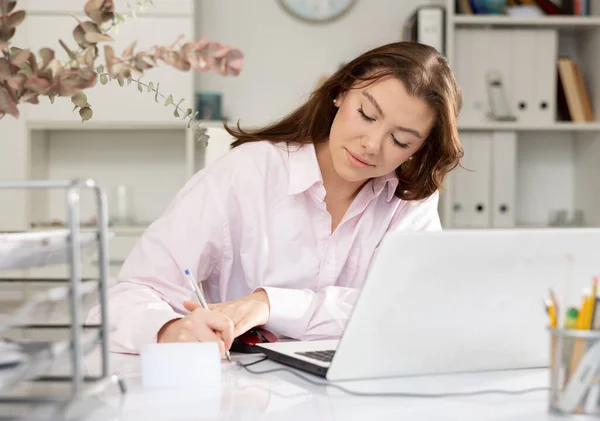 彼女の職場でテーブルに座って紙に書いている女性のブックキーパー — ストック写真