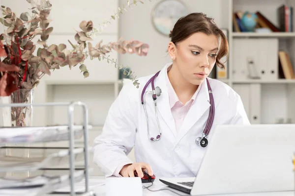 女医生坐在办公室工作台旁使用笔记本电脑的外科刷子的画像 — 图库照片