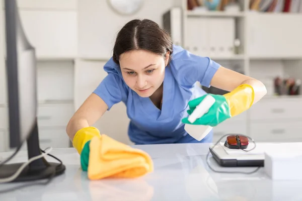 Cleaning company employee wipes dust from table in office