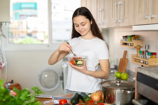 年轻的家庭主妇在家里厨房里用盘子吃蔬菜沙拉 — 图库照片