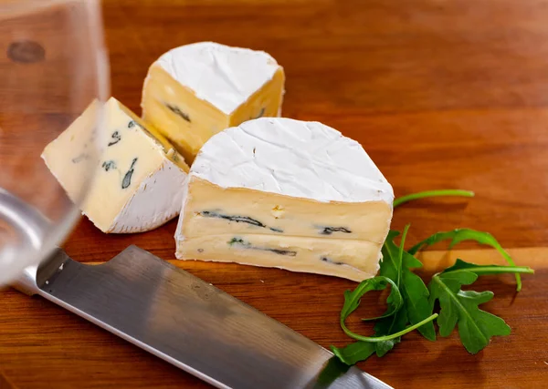 木製のテーブルの上にナイフと新鮮なアルグラの葉で高貴な青カビと職人の豊かでクリーミーなチーズのスライス — ストック写真