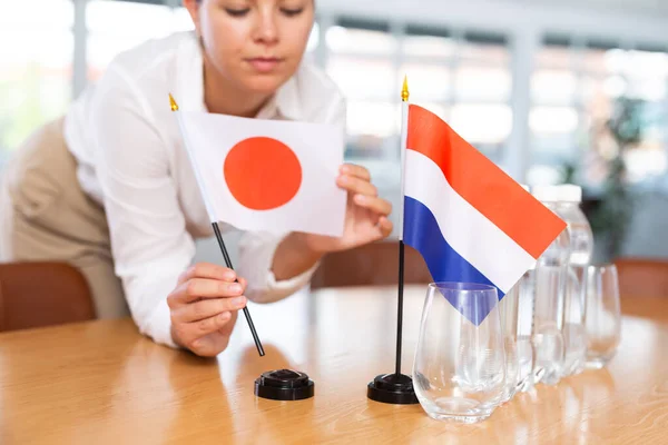 ビジネス服の若い女性は オフィスで交渉テーブルに日本とオランダの旗を置く — ストック写真