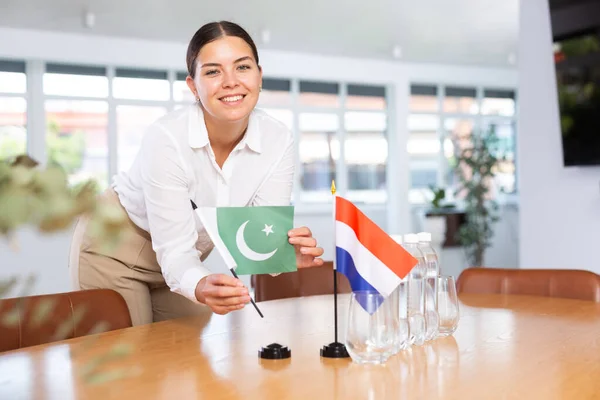 助理女孩为国际谈判和领导人会议准备办公室 女士把荷兰和巴基斯坦的迷你国旗摆上桌 后续行动 — 图库照片