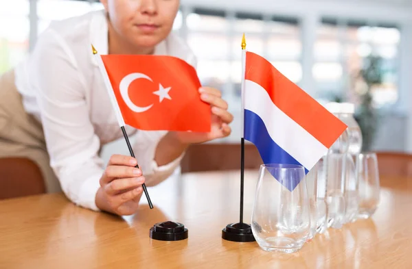 女性秘書は交渉のためのオフィスを準備します 彼女はトルコとオランダの旗を置きます — ストック写真