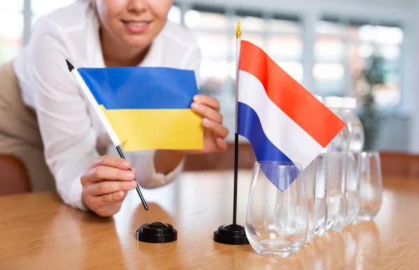 难以辨认的妇女为国际谈判和领导人之间的沟通讨论准备了空间 女士把荷兰和乌克兰的小国旗摆上桌 无重点射击 — 图库照片