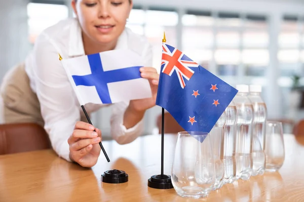 身穿商务服装的年轻女性把芬兰和新西兰的国旗摆上谈判桌 — 图库照片