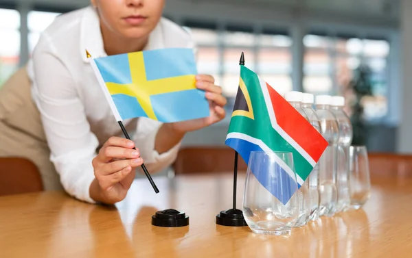 难以辨认的妇女为国际谈判和领导人之间的沟通讨论准备了空间 女士把南非和瑞典的小型国旗摆上桌 无重点射击 — 图库照片
