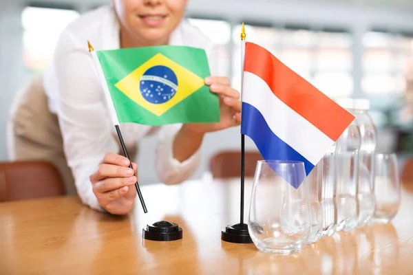 女性秘書は交渉のためのオフィスを準備します 彼女はオランダとブラジルの旗を置きます — ストック写真