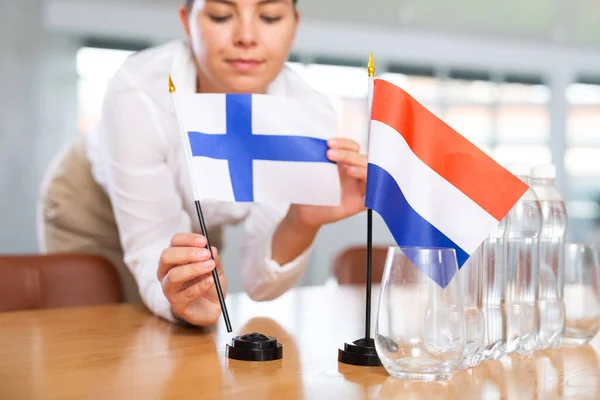 身穿商务服装的年轻女性把芬兰和荷兰国旗摆上谈判桌 — 图库照片