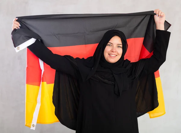 ドイツの旗を掲げる黒い伝統的なヒジャブを身に着けている陽気な若いイスラム教徒の女性 — ストック写真