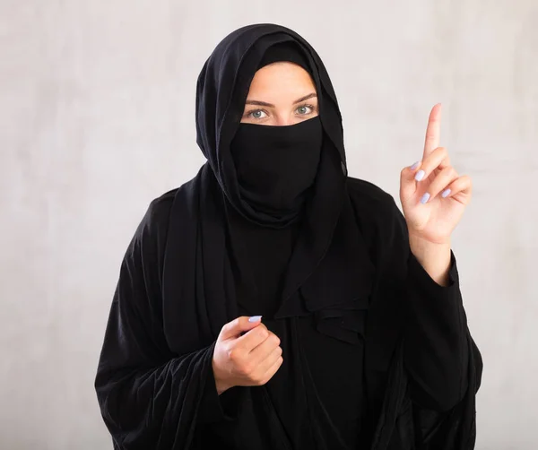 身穿黑色传统面纱的年轻的穆斯林女士指着旁边说话 — 图库照片