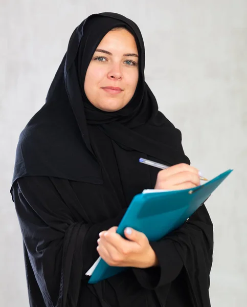 穿着伊斯兰传统服装拿着课本的年轻女生笑着 — 图库照片