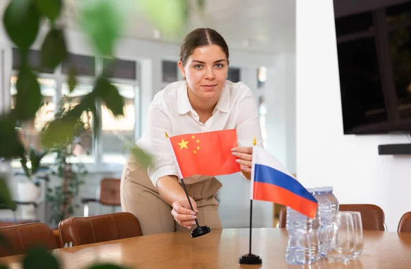 Egy Fiatal Üzleti Ruhában Kínai Orosz Zászlókat Tesz Tárgyalóasztalra Irodában — Stock Fotó