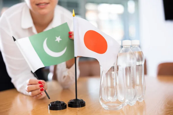 将巴基斯坦和日本的国旗放在女办公室秘书的手中 为国际谈判准备会议室的餐桌 有选择地突出重点 外交伙伴关系的概念 — 图库照片