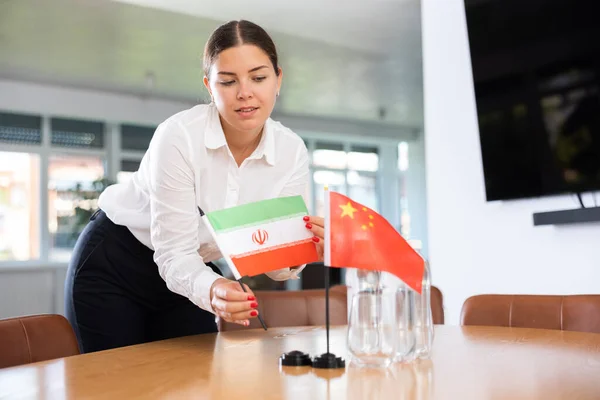 Assistant girl prepares office for international negotiations and meetings of leaders. Lady sets miniatures flags of China