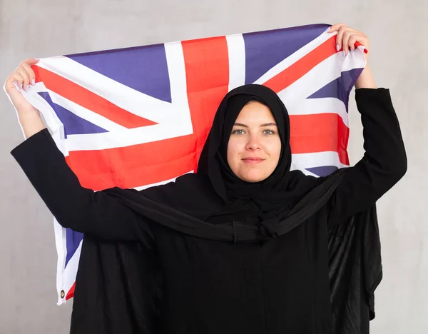 イギリスの国旗を掲げる黒い伝統的なヒジャブを身に着けている陽気な若いイスラム教徒の女性 — ストック写真